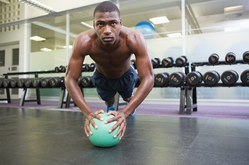 Determined shirtless muscular man doing push ups with ball in the gym