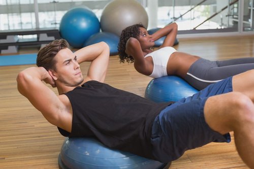 Couple doing sit ups on exercise balls at the gym
