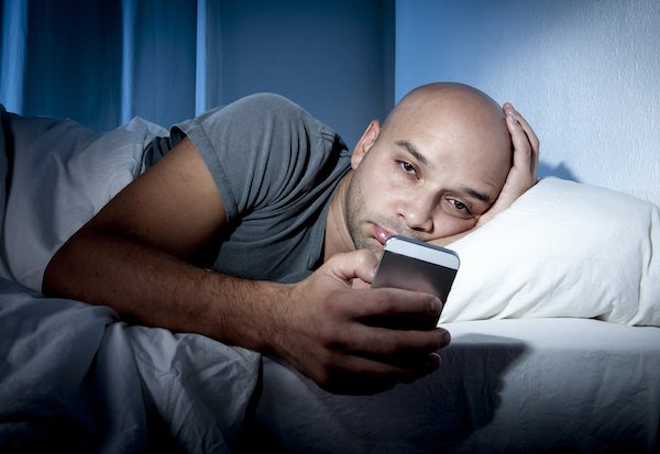 young cell phone addict man awake at night in bed using smartphone