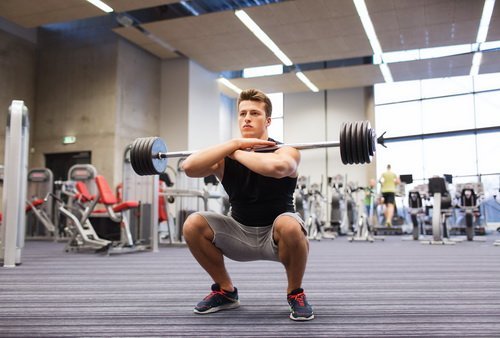 young man flexing muscles with barbell in gym