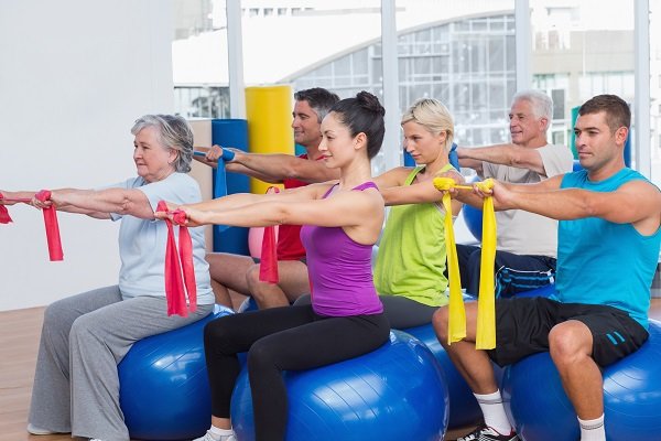 Men and women on fitness balls exercising with resistance bands in gym