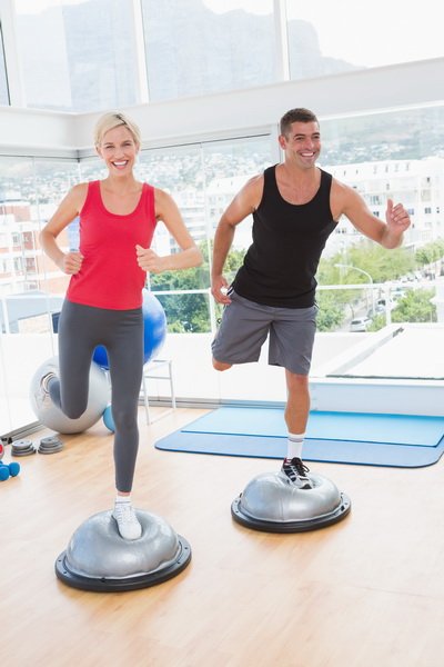 Fit couple working on bosu ball in fitness studio