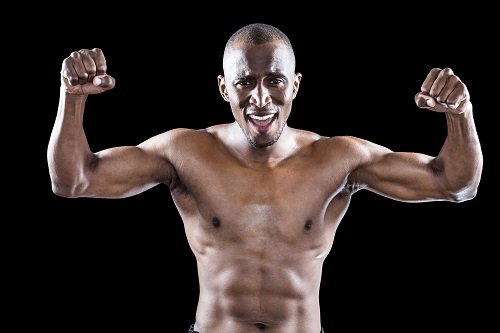 Portrait of happy shirtless athlete cheering while standing on black background