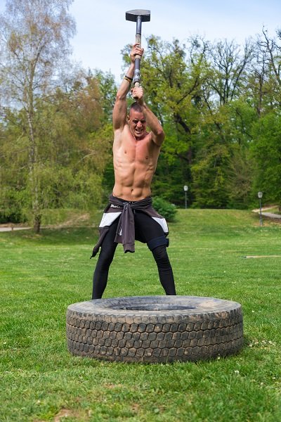 年轻的运动员在公园里训练，用大锤和卡车轮胎作为体能训练的一部分