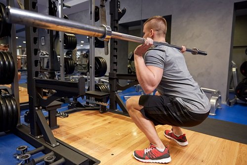 young man flexing muscles with bar in gym